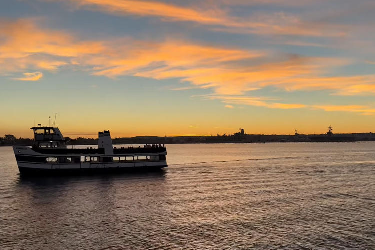 Ferry on calm water at sunset with orange and blue sky.
