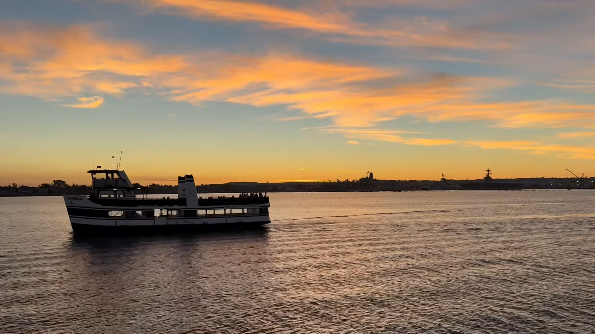 Ferry on calm water at sunset with orange and blue sky.
