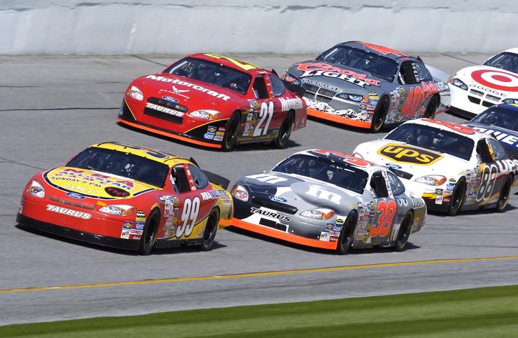 Stock cars racing closely together on a track.